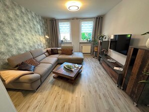 Ein Wohnzimmer mit Ecksofa, Couchtisch, Flachbildfernseher und Kamin.