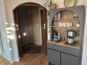 Eine moderne Küche mit einer Kaffeestation, einer Holzküche mit Regalen und einer Tür zu einem weiteren Raum.