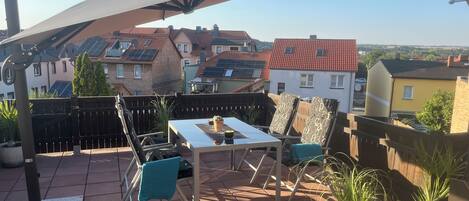 A terrace with a table and chairs, a pergola, and potted plants.