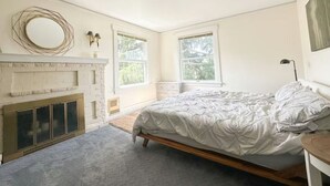 Quarto com cama, lareira e duas janelas.