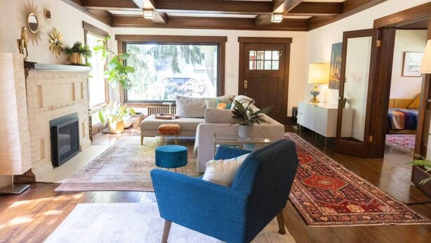Uma sala de estar com lareira, um sofá, uma poltrona azul e um tapete estampado.