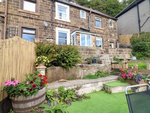 A residential property with a stone facade, multiple windows, a wooden fence, and a variety of potted plants.