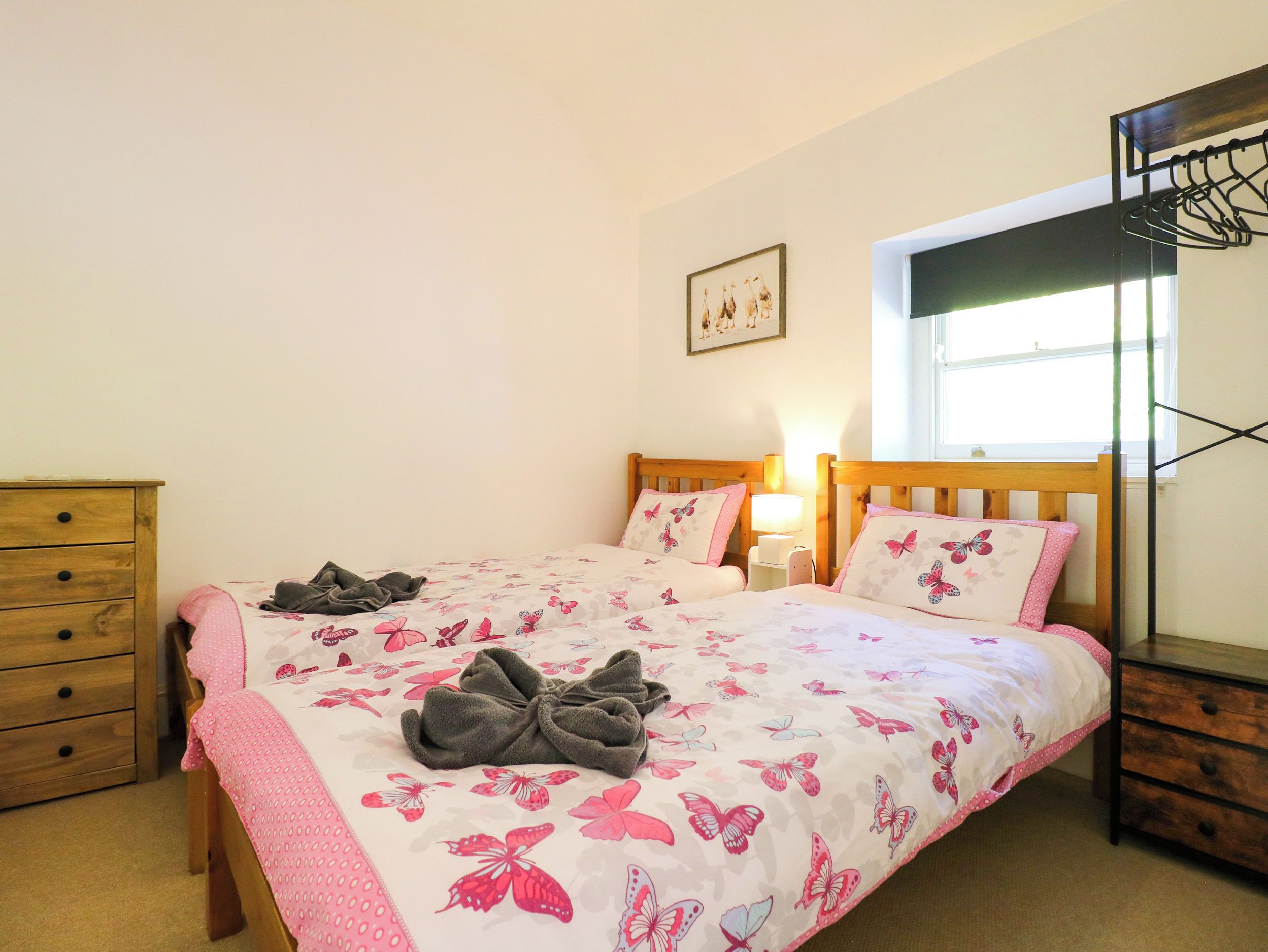 Un dormitorio con cama, cómoda, mesita de noche, lámpara, ventana y estante en la pared.