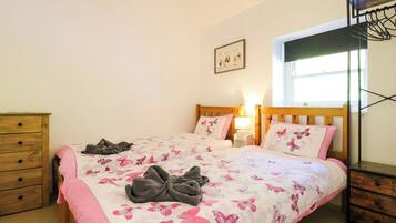 Un dormitorio con cama, cómoda, mesita de noche, lámpara, ventana y estante en la pared.