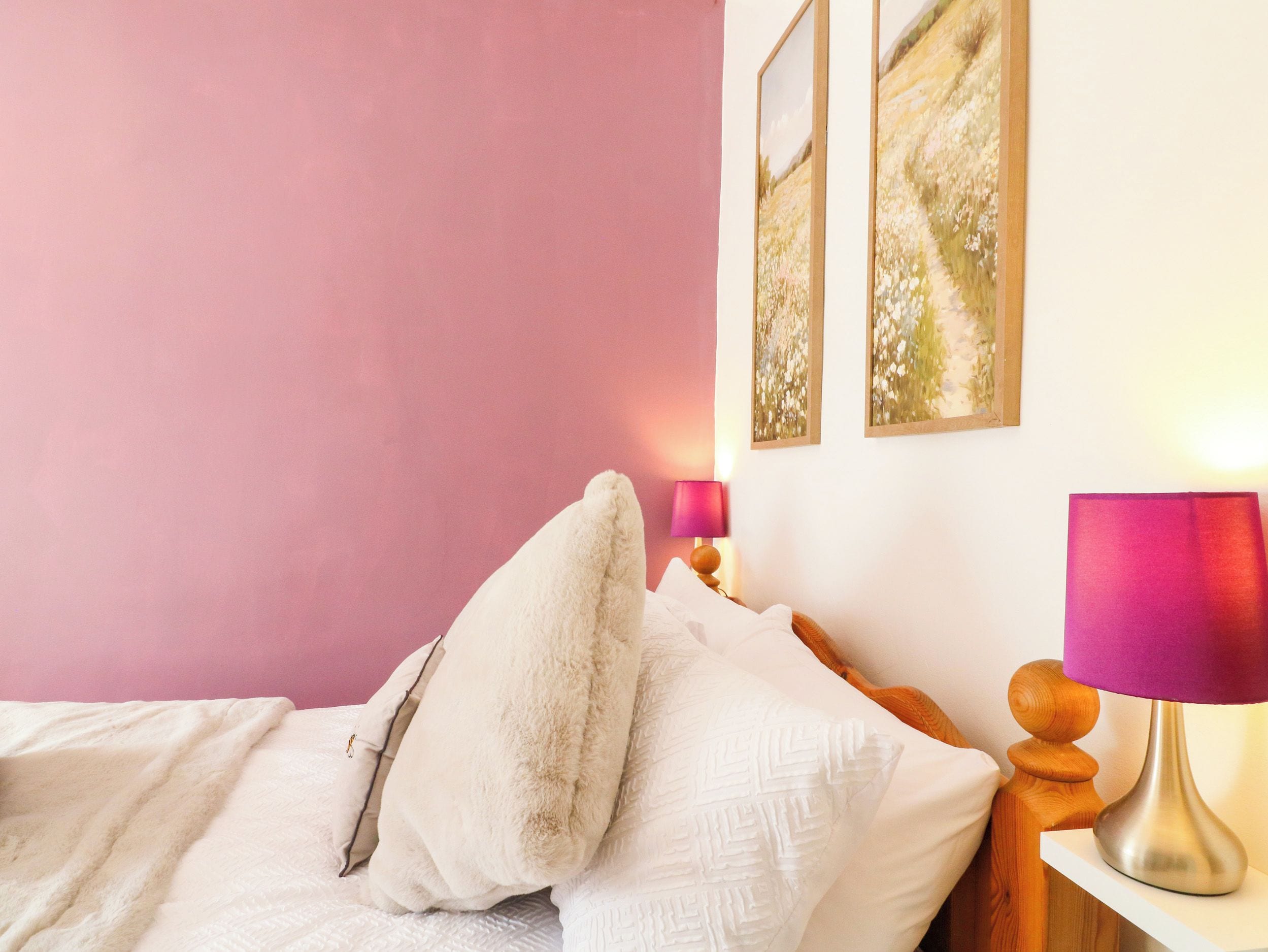 A bedroom with a bed, pillows, a bedside table with a lamp, and wall art.