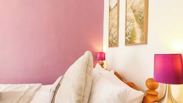 A bedroom with a bed, pillows, a bedside table with a lamp, and wall art.