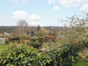Ländliche Landschaft mit einer hölzernen Bank, einer kleinen Scheune und einer Ferne mit Häusern und Hügeln.