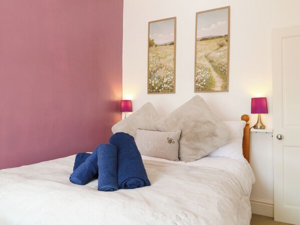 A neatly made bed with rolled towels, a pillow with a bee design, and two framed pictures on the wall.
