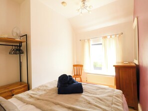 A bedroom with a bed, a chair, a radiator, and a window with curtains.