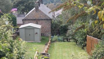 A stone house with a small shed, surrounded by a wooden fence and lush greenery.