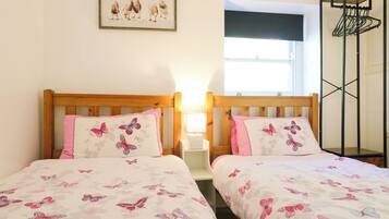 A room with two beds, each with a pillow featuring butterfly designs, a framed picture on the wall, and a window with a view.