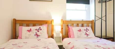A room with two beds, each with a pillow featuring butterfly designs, a framed picture on the wall, and a window with a view.