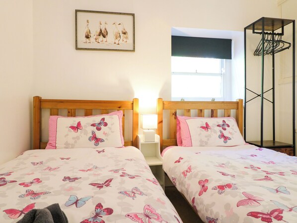 A room with two beds, each with a pillow featuring butterfly designs, a framed picture on the wall, and a window with a view.