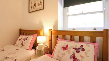 Un dormitorio con dos camas, cada una con un cojín floral y una mesita de noche con lámpara.
