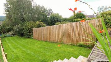 Un jardín bien cuidado con cerda de madera, césped y una terraza de madera.