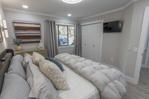 Un dormitorio con cama, televisión, ventana con cortinas, un cuadro y una estatua.