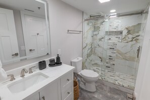 Un baño moderno con tocador blanco, cabina de ducha de vidrio y salpicadero de mármol.