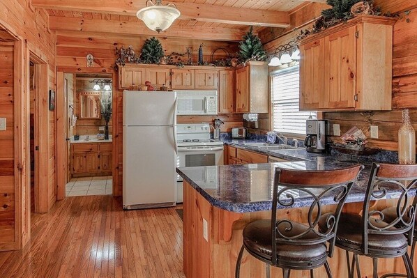 A wooden cabin-style kitchen with a refrigerator, microwave, stove, and bar seating. - Soaring Eagle 4 Bedroom Cabin (Pigeon Forge)