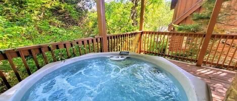 A hot tub surrounded by a wooden deck and a wooden fence, with trees in the background.