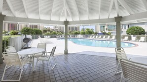 Un área de piscina techada al aire libre con suelo de baldosas, sillas y mesas de metal blanco.