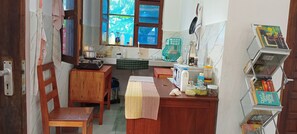 A compact kitchen with a wooden table, a window with a view, a shelf with books, and a small countertop with jars.