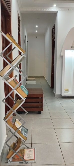 A hallway with a metal bookshelf, a wooden bench, and a tiled floor.