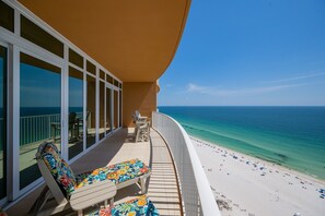 Ein Balkon mit Blick auf den Ozean, einen Strand und einen Poolbereich mit Liegestühlen.