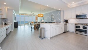 Una cucina moderna con mobili bianchi, un'isola grande, elettrodomestici in acciaio inossidabile e un'area pranzo con vista.