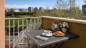 En balkon med et bord dækket til et måltid, inklusive en kop kaffe, et croissanter og en potteplante.
