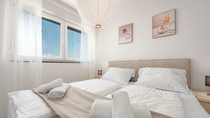 A neatly made bed with white linens and a beige throw blanket, a bedside lamp, and two framed pictures on the wall. - New vacation home in Nin, 100m to the beach l 3 bedrooms l 2 bathrooms l 6 pers. l All-inclusive. (Nin)