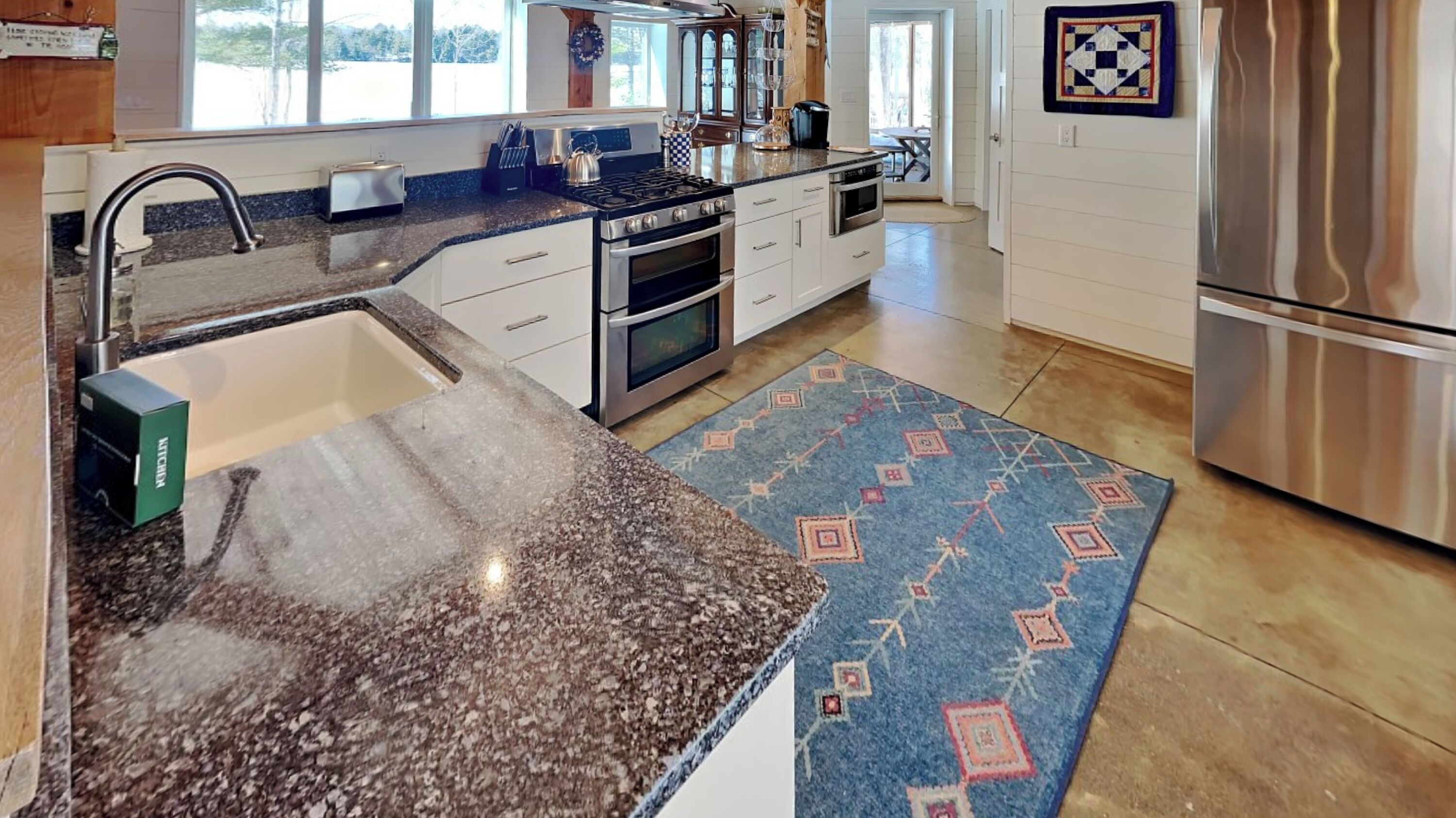 A kitchen with granite countertops, stainless steel appliances, and a patterned rug.