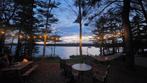 An outdoor dining area with a view of a lake, surrounded by trees and string lights.