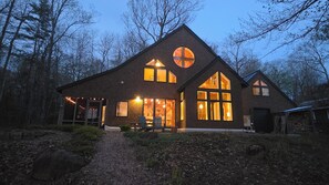 A wooden house with large windows, a porch, and a gravel path.