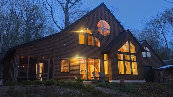 A wooden cabin with large windows, a circular skylight, and a porch with chairs.