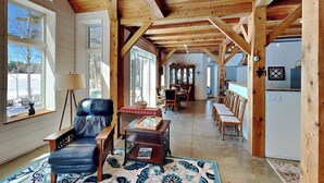 Une pièce spacieuse avec un plafond en bois, un fauteuil en cuir, une table à manger et un coin cuisine équipé d’un réfrigérateur.