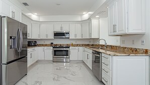 Una cocina moderna con gabinetes blancos, electrodomésticos de acero inoxidable y piso de mármol.