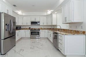 A modern kitchen with white cabinets, stainless steel appliances, and a marble floor. - Waterfront Oasis in Jensen Beach – 3BR • 2.5BA • Private Dock • Walk to Beach (Jensen Beach)