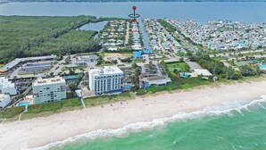 Vista aérea de un complejo turístico costero con propiedades frente a la playa, un hotel central y un puerto deportivo.