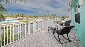 Un balcón con vistas a una zona residencial, una piscina y un cielo despejado.