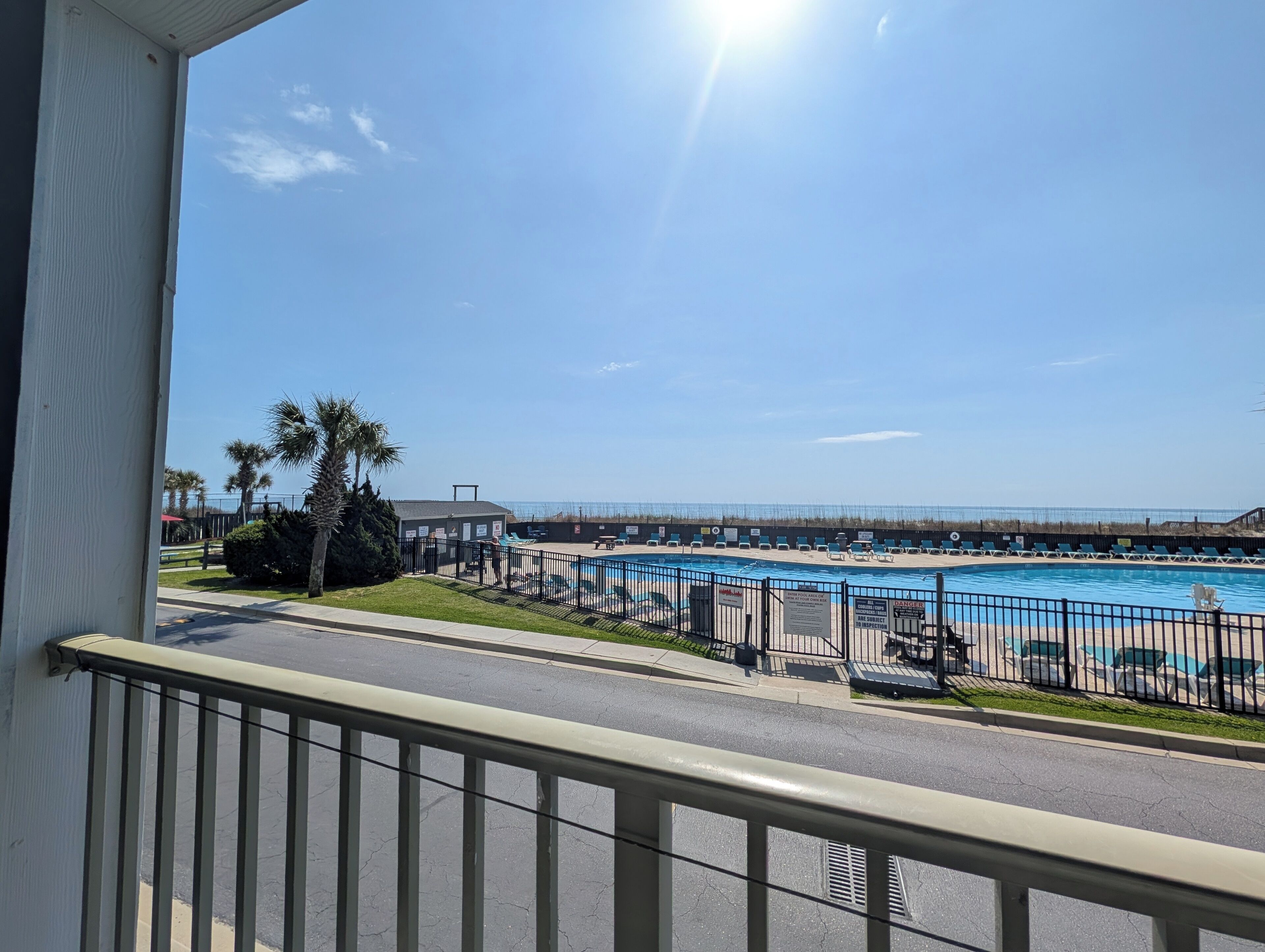 En pool med utsikt över stranden, ett inhägnat område och en byggnad i bakgrunden.