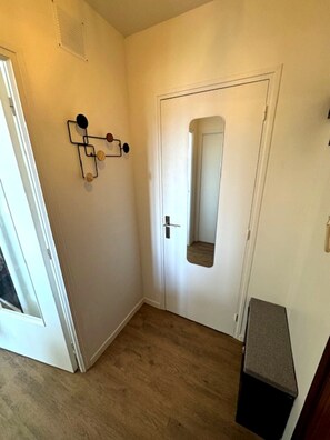 A hallway with a white door, a mirror, and a small black object on the wall. - Apartment with south-facing balcony - 200 m from the beach - Thalasso - Casino (Ouistreham)