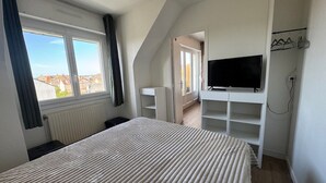 Et soveværelse med seng, fjernsyn, radiator og et vindue med gardiner.