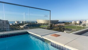Ein Schwimmbecken mit Glasbarriere, Blick auf ein modernes Gebäude und ein klarer Himmel.