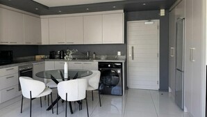 Eine moderne Küche mit weißen Schränken, einem runden Esstisch mit Stühlen, einer integrierten Waschmaschine und einem Kühlschrank.