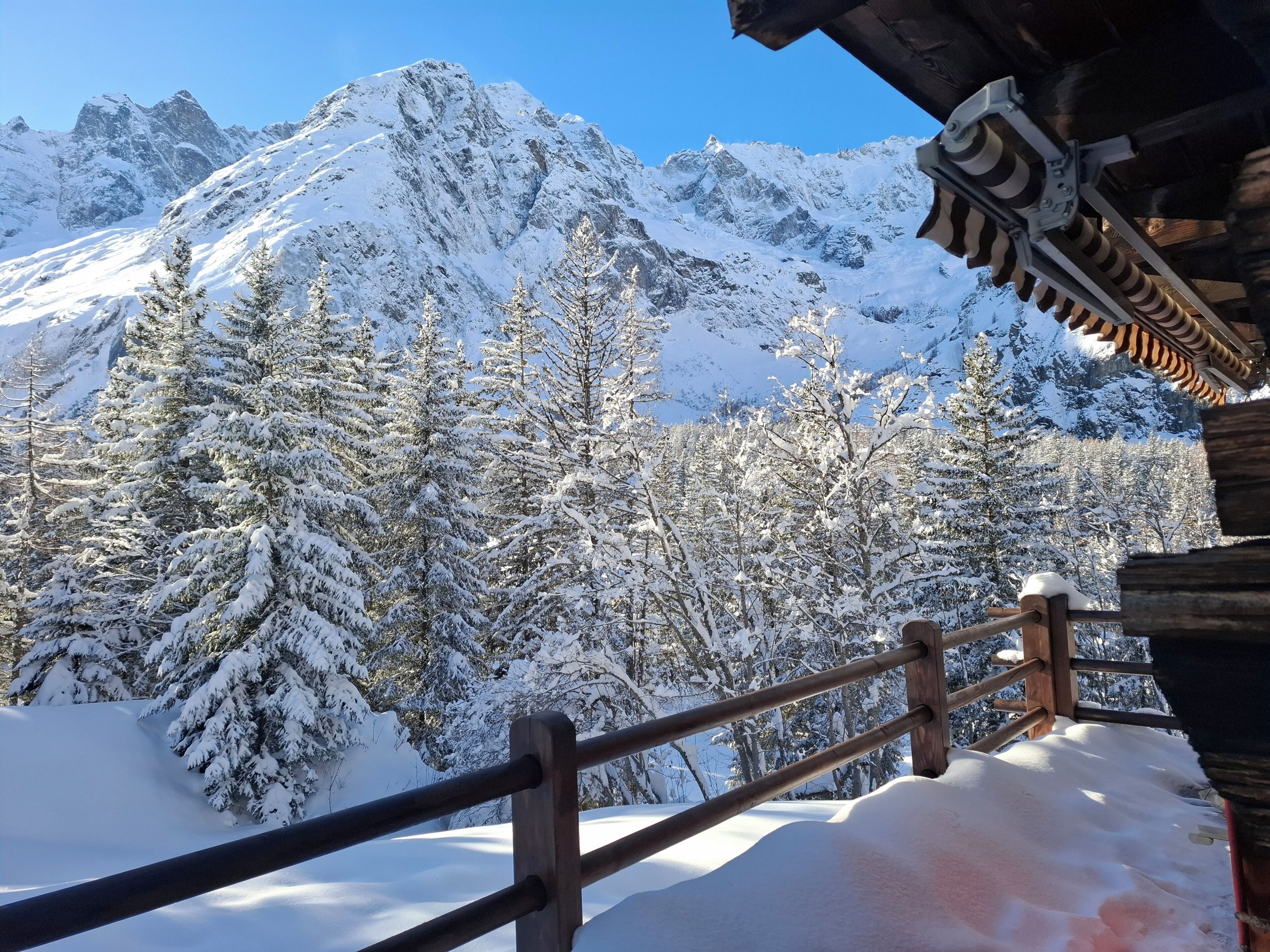 A wooden balcony with a metal railing overlooking a snow-covered mountain landscape.