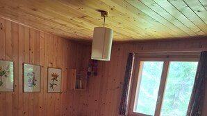 Ett sovrum med träpanel på väggarna, en säng, ett fönster och inramade blomstermotiv på väggen.