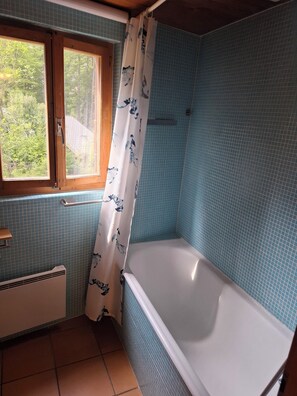 Et badeværelse med et badekar, et vindue med træramme og blå flisemure.