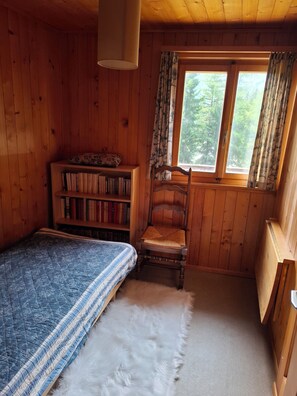 Et hyggeligt træhytteværelse med seng, reol, stol og et vindue med gardiner.