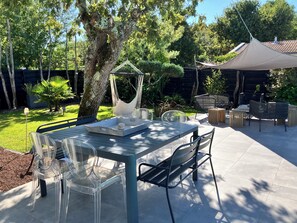 A patio with a table and chairs, surrounded by trees and a covered area. - Villa Charmence Ideal, quiet location 100M from the beach and oyster port (Andernos-les-Bains)