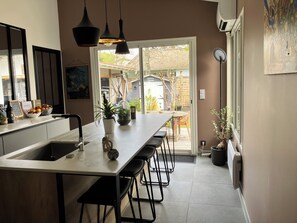 A modern kitchen with a central island, pendant lights, and a view to the backyard. - Villa Charmence Ideal, quiet location 100M from the beach and oyster port (Andernos-les-Bains)